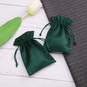 Close-up of dark green velvet drawstring jewelry pouches with soft texture on white wood