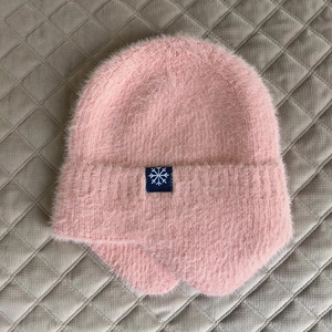 Dettaglio del berretto in peluche rosa con consistenza morbida e patch a fiocco di neve