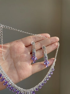 Detailed view of rhinestone fringe necklace and purple teardrop earrings set being held