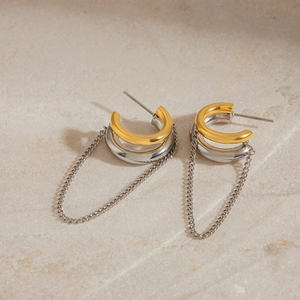 Detail view of gold-plated C-shaped hoop earrings with silver tassel chain on stone surface