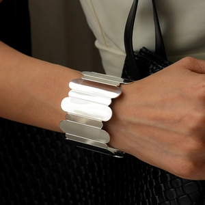 Close-up of a wide silver wave-edged metal cuff bracelet on a model's wrist
