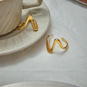 Vue rapprochée des boucles d'oreilles dorées en forme de vague sur un lin blanc