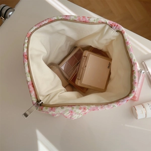 Floral quilted makeup bag with wide opening showing cosmetics inside on a white desk