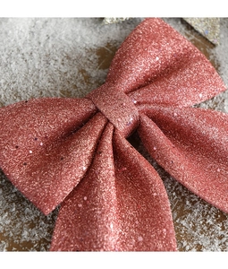 Macro detail of rose gold glitter Christmas bow decoration on snow-covered wood surface