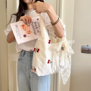 Detail of white tulle canvas bag with cherry embroidery and large lace bow decoration