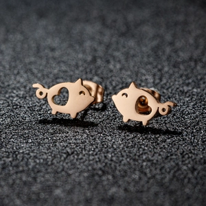 Cute rose gold pig stud earrings with hollow heart detail on black glitter background