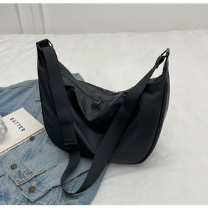 Detail of minimalist black nylon dumpling bag with adjustable wide strap on white fabric