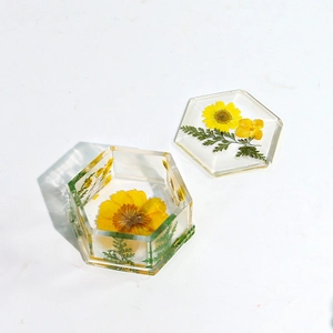 Detalle de caja hexagonal de resina con margaritas amarillas y hojas de helecho verdes