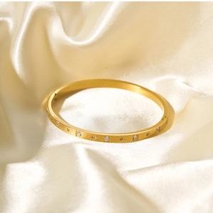 Dettaglio di un bracciale rigido placcato oro 18k con zirconi su seta champagne