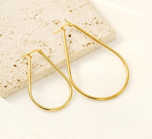 Macro view of gold teardrop earrings with a polished finish on stone background
