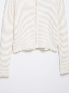 Détail d'un cardigan blanc en maille avec finitions élégantes en perles sur les bords