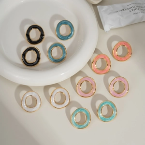 Détail de boucles d'oreilles créoles en émail coloré et finition dorée sur fond beige