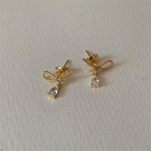 Elegant gold bow earrings with pear-cut cubic zirconia on a cream textured surface