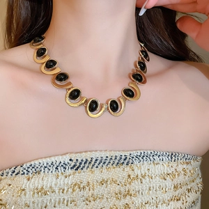 Close-up of a gold wave chain necklace featuring oval black stones on a model