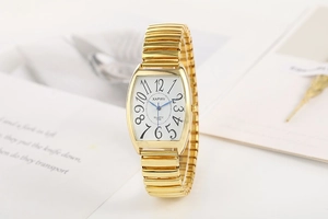 Détail d'une montre tonneau dorée avec aiguilles bleues et bracelet élastique en acier
