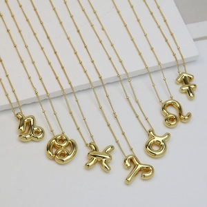 Detailed view of 3D chubby balloon zodiac necklaces in polished gold finish on white stone
