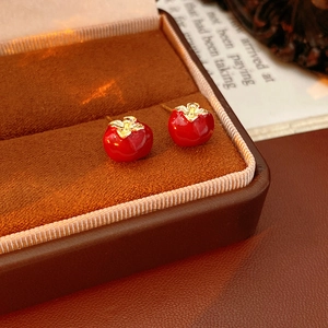 Macro shot of red persimmon stud earrings with gold details in a luxury velvet box