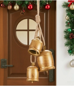 Three vintage golden Christmas cow bells hanging on jute rope against a festive wooden door