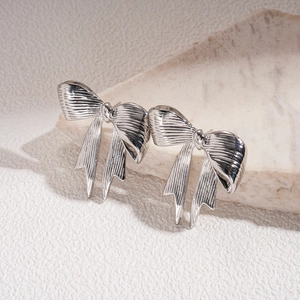 Macro detail of silver bow earrings with smooth metallic texture and 3D ribbon design