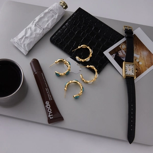 Detailed flat lay of gold-finished C-hoop earrings with turquoise and pearls on a grey laptop