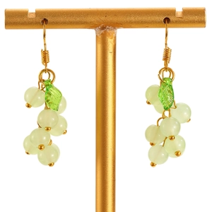 Detail of green grape pendant earrings hanging on a gold jewelry display stand