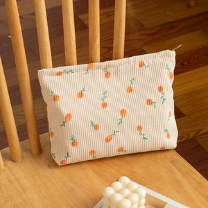Detail of floral corduroy makeup bag with orange pattern on a wooden chair