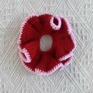 Detailed macro view of handmade crochet scrunchie with red cotton yarn and pink ruffle edges