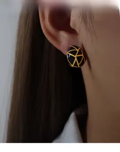Close-up of elegant black enamel drop earrings with gold geometric lines on female model