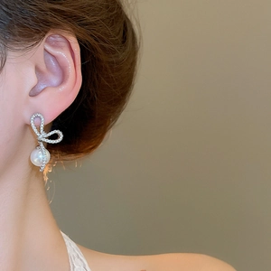Close-up of silver bow stud earrings with sparkling crystals and a white round pearl