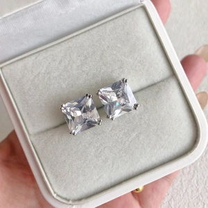 Close-up of square cut zircon earrings in silver four-prong setting on a beige velvet box
