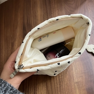 Detailed view of cream corduroy heart-print makeup bag with cosmetics on a wooden table