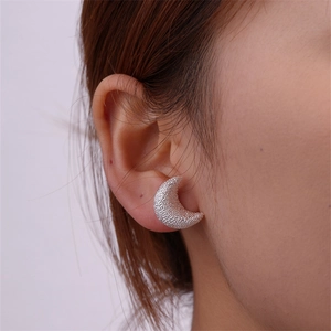 Close-up of crescent moon stud earrings with frosted texture worn by a female model