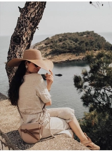 Détail d'un chapeau de paille à larges bords et d'un ensemble en lin avec sac beige
