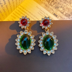 Orecchini vintage a girasole con pietre rosse e verdi su pagine di vecchi libri
