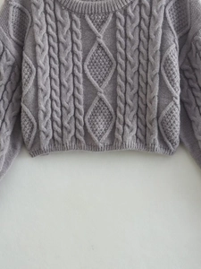 Dettaglio del maglione grigio con motivo a rombi e trama a treccia a maglia fitta