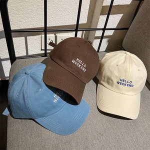 Three embroidered baseball caps in light blue, brown and beige on fabric surface