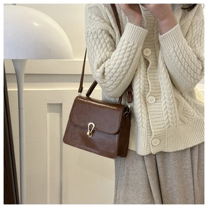 Detail of dark brown vintage PU leather crossbody bag with metallic buckle and flap