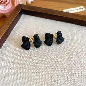 Elegant matte black bow earrings with gold accents on a stylish neutral jewelry display tray