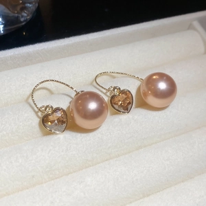Detail view of heart-shaped champagne zircon and large pink-gold pearl earrings in box