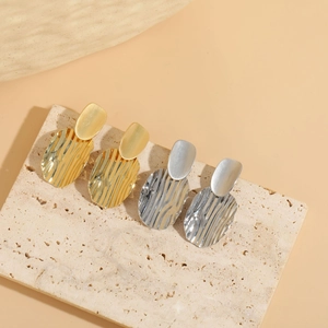Macro view of gold and silver textured hoop earrings on a minimalist beige stone background