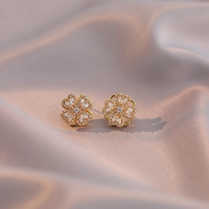 Orecchini a fiore dorati con micro-pavé di zirconi su sfondo di seta morbida ed elegante