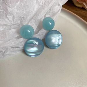 Detail of round light blue resin stud earrings with iridescent mother-of-pearl shell texture