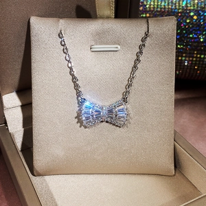 Detailed view of silver bow necklace with zircon stones in a beige jewelry box
