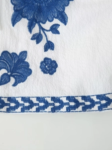 Detailed view of intricate blue floral embroidery on white fabric of this vintage cardigan