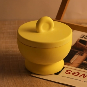 Dettaglio ravvicinato di un barattolo rotondo in ceramica gialla opaca con coperchio