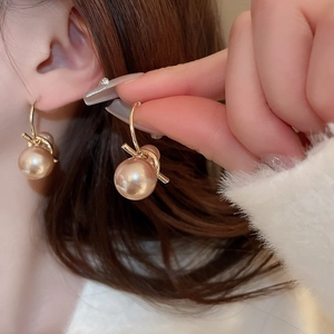 Gros plan sur d'élégantes boucles d'oreilles nœud d'or et perles portées par un mannequin