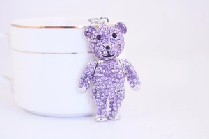Macro shot of purple crystal teddy bear keychain leaning on a white gold-rimmed teacup