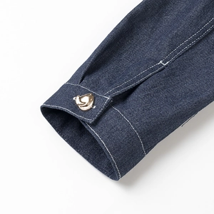 Détail de manche en denim bleu foncé avec surpiqûres blanches et bouton doré de luxe