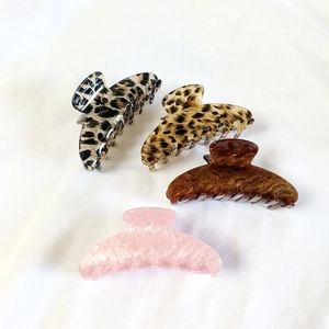 Detail of four acetate hair claw clips in leopard print and marble patterns on white fabric