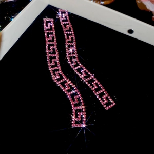 Dettaglio macro di lunghi orecchini a nappa in oro rosa con strass rosa e motivo a greca
